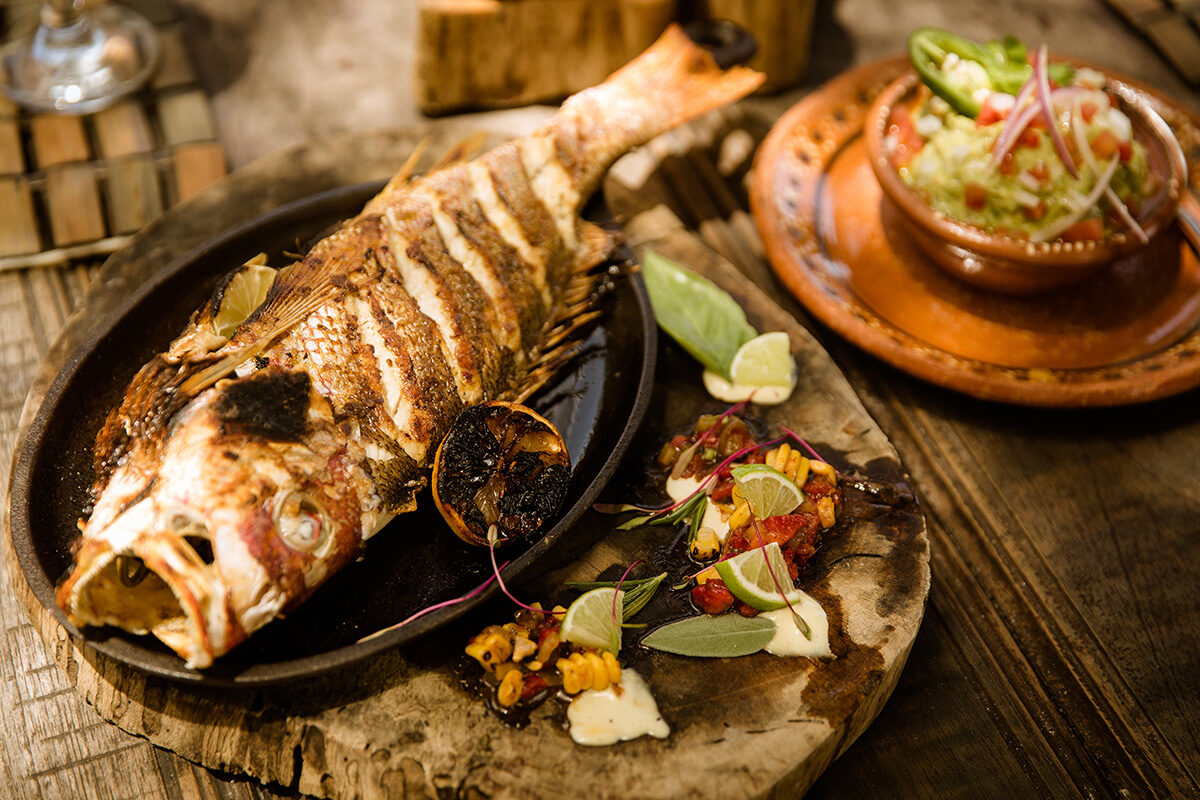 Whole grilled fish on wooden board with guacamole side, Tulum-style