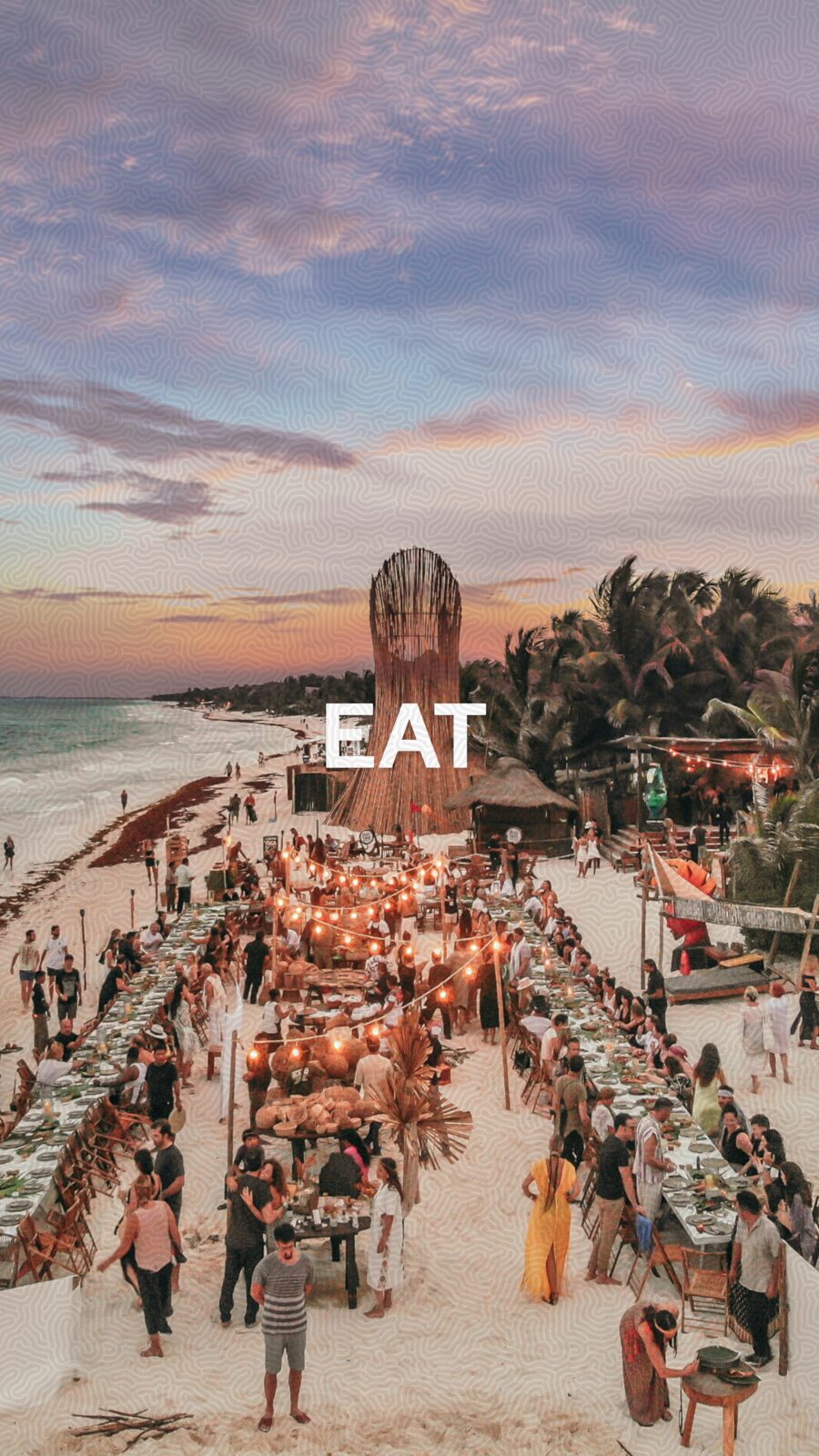 Long communal dinner tables on Tulum beach at sunset, hundreds of guests, bamboo tower installation