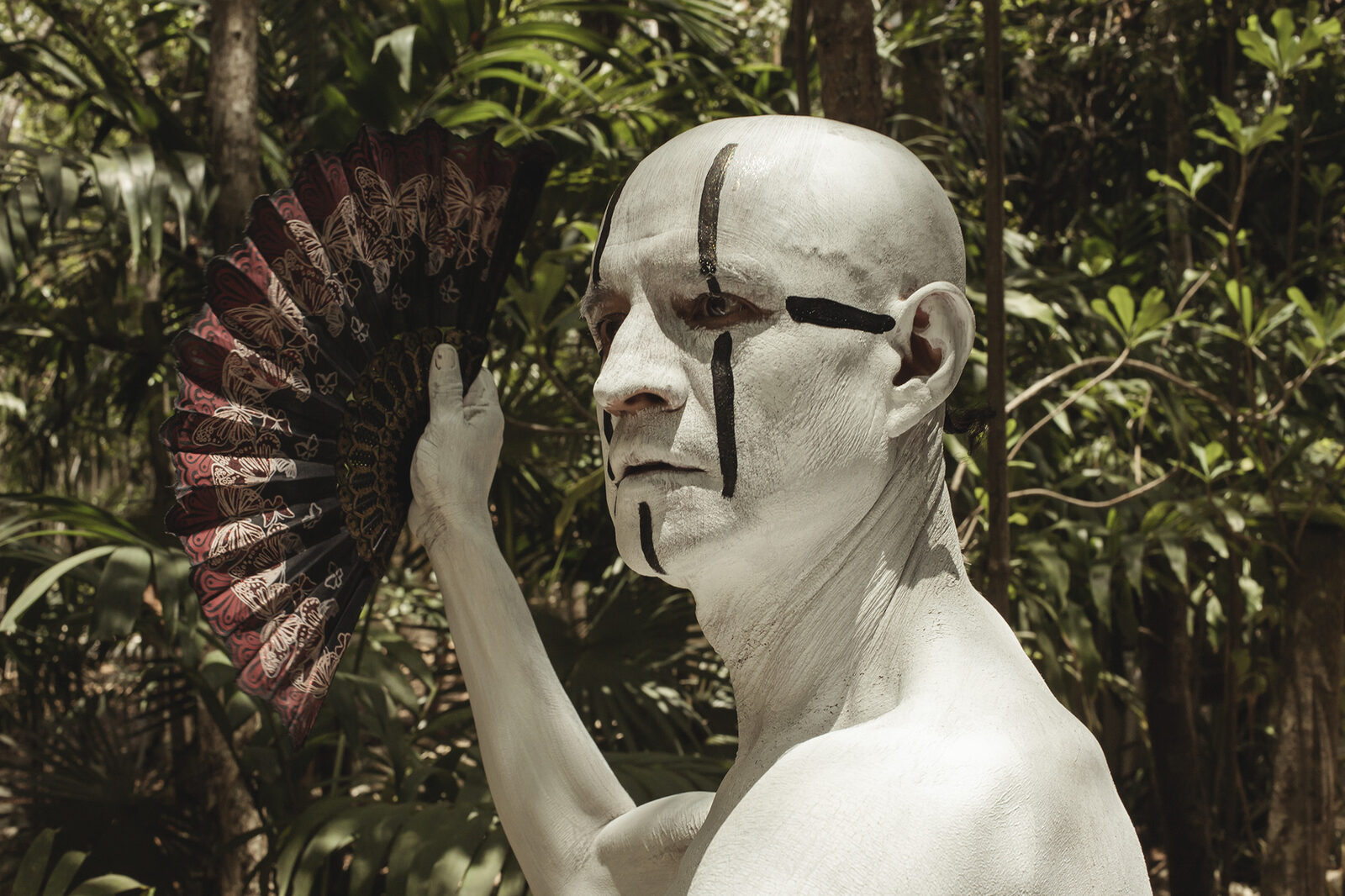 Performer in white body paint with butterfly fan in Tulum jungle