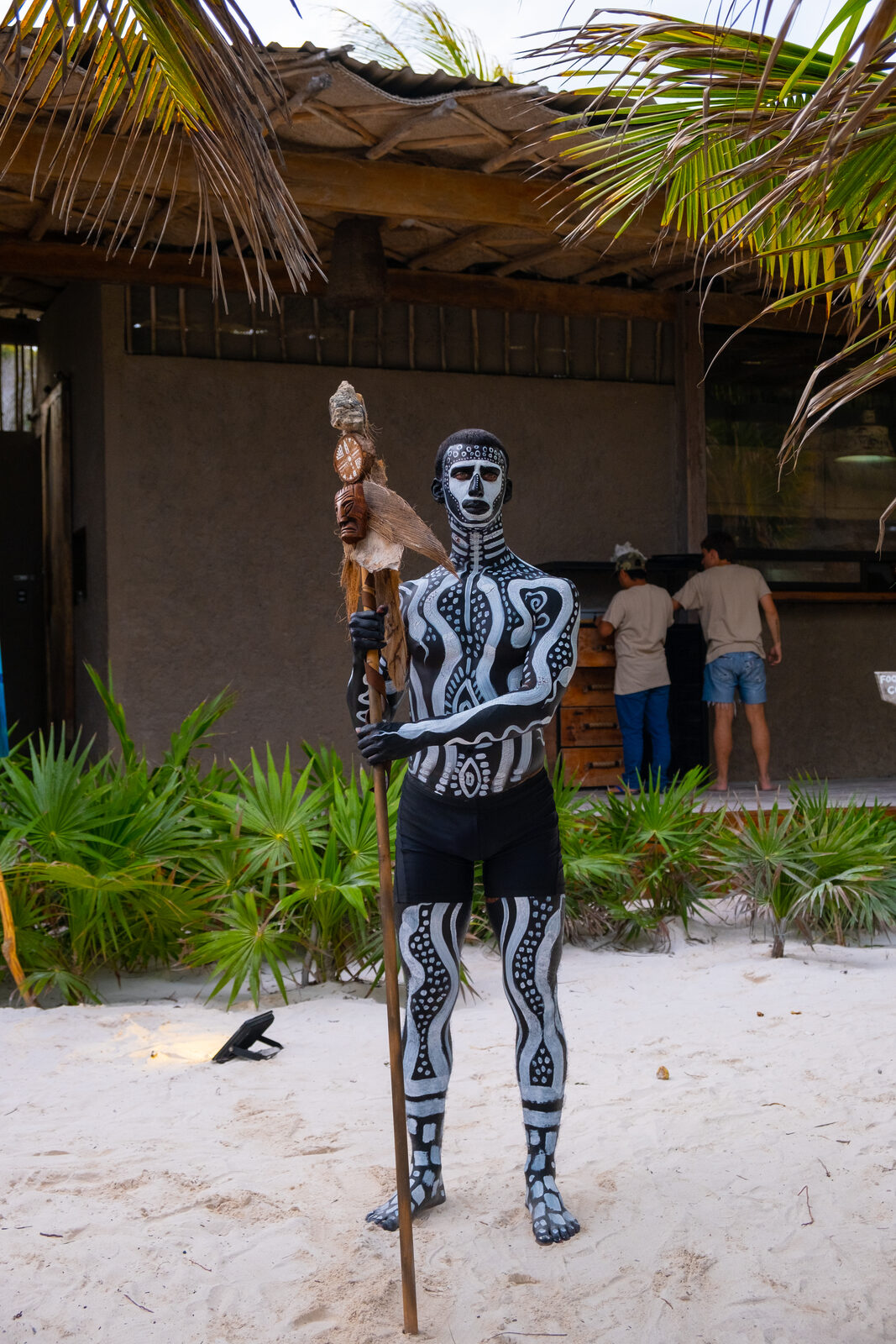 Body-painted performer with ceremonial staff on Tulum beach